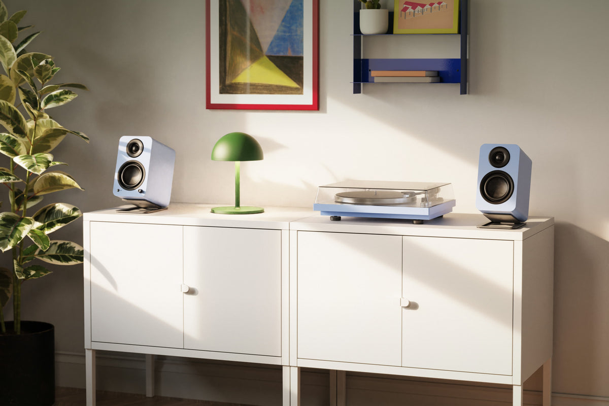 A white modern cabinet, styled in a room with a plant, YU4 speakers, a green lamp, and a record player on top.