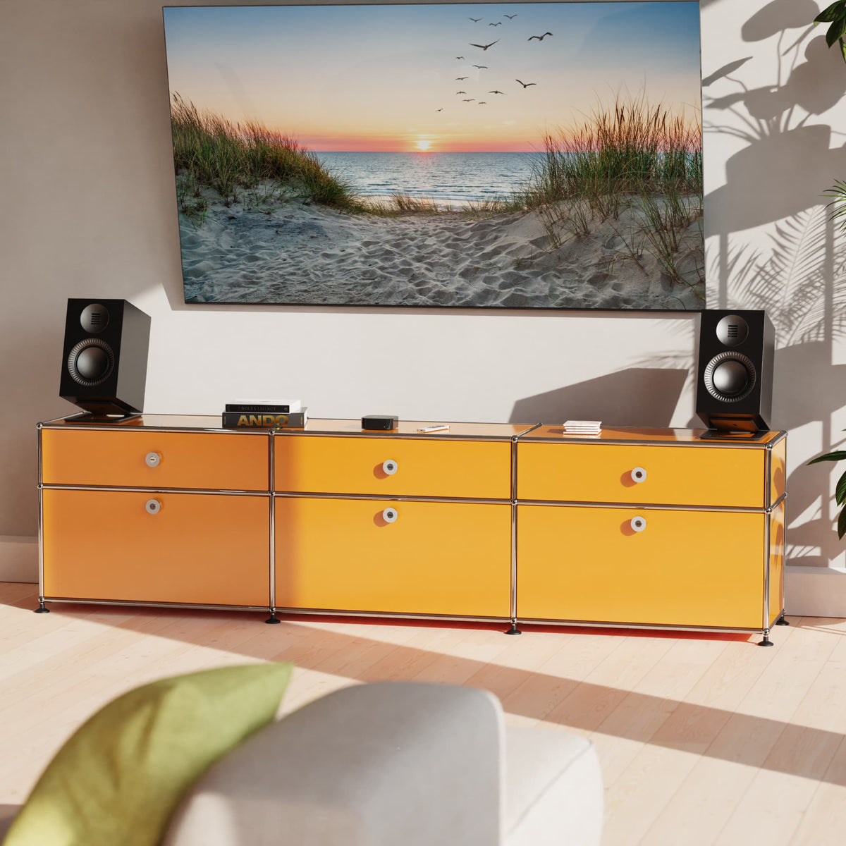 A modern yellow and orange modular media console with chrome legs and drawer knobs, styled in a living room setting with speakers on Kanto S6 mounts, a TV on the wall, and a sofa in the foreground.