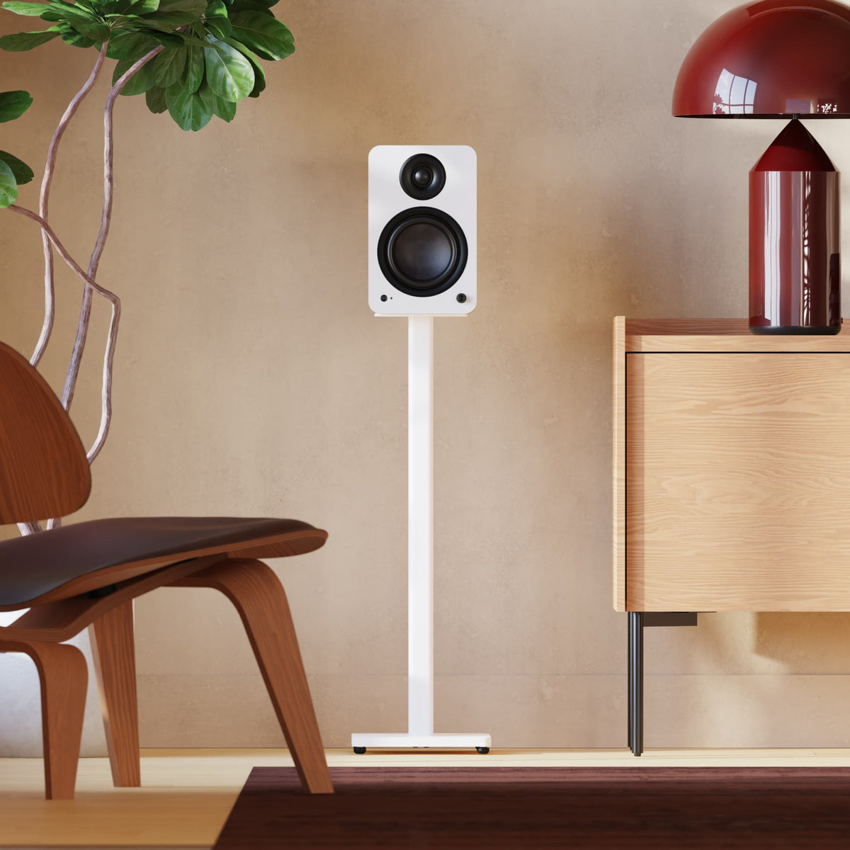 A white floor-standing speaker on a slim Kanto SP32 white stand, shown in a modern room setting with a wooden chair, plant, and cabinet.