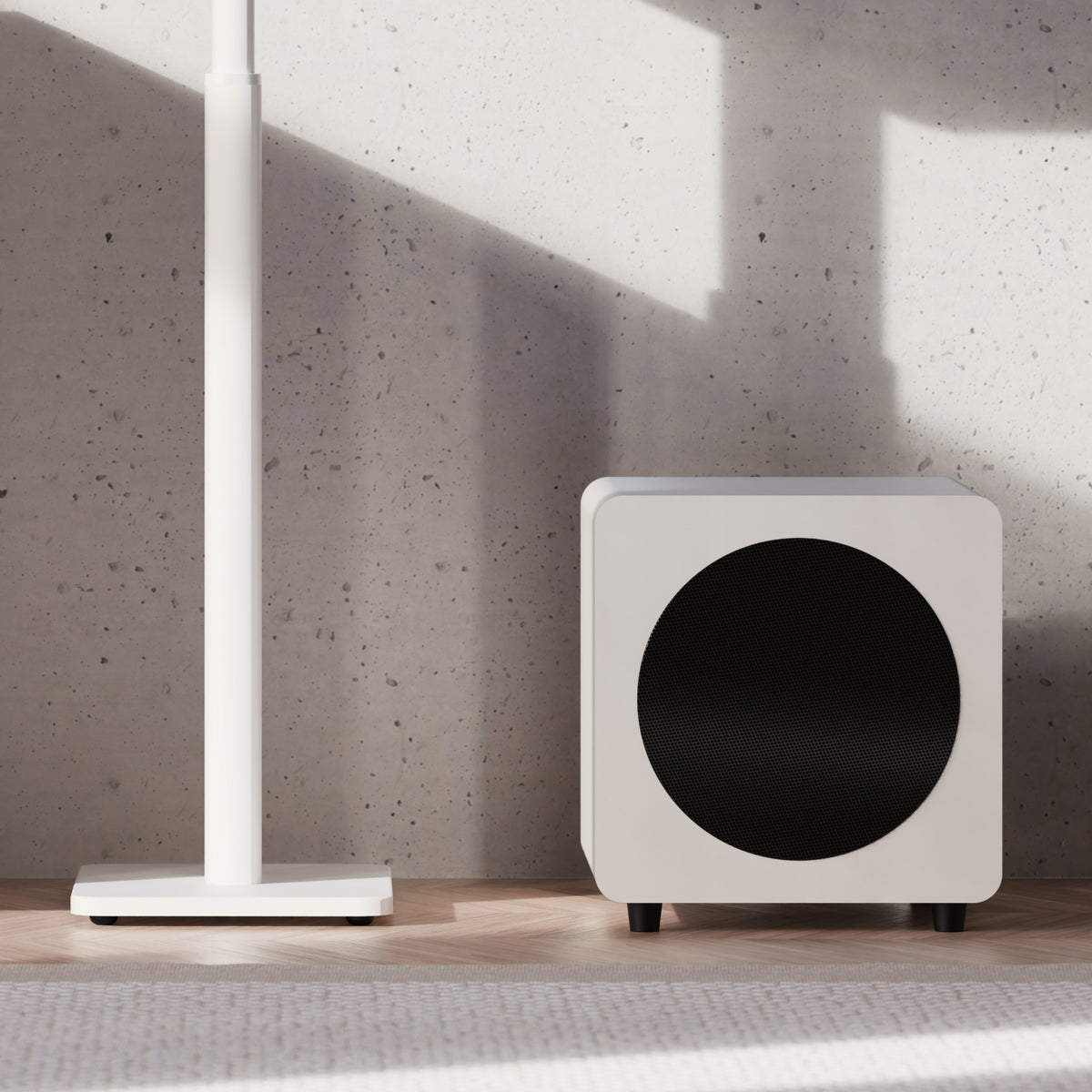 A Kanto Sub8 subwoofer, placed on a light wood floor against a textured concrete wall with strong sunlight shadows.