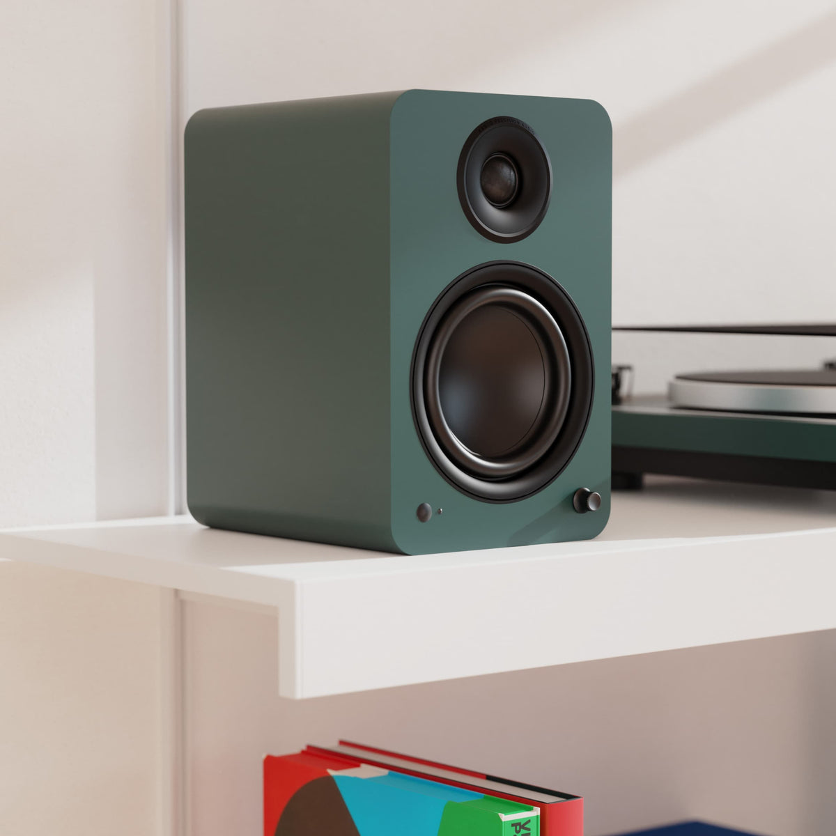 A Yu6 dark green rectangular speaker with black drivers sits on a white shelf in a clean indoor setting.