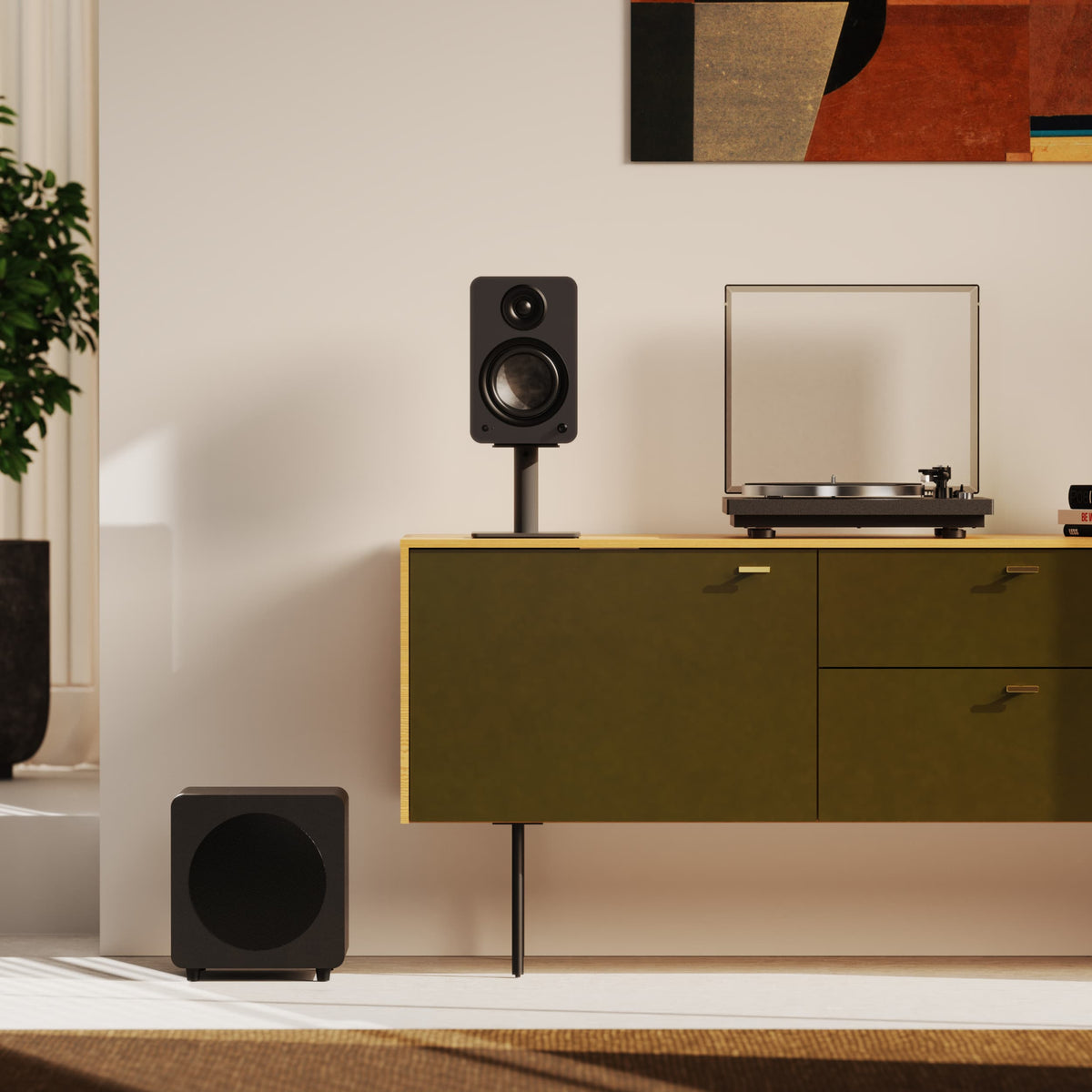 A modern room scene showing a black Yu6 speaker on an olive green cabinet, with a turntable beside it and a matching black subwoofer on the floor. A cream wall, framed abstract art, and a plant are visible in the background.